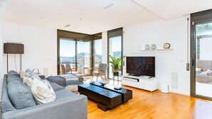 Ein modernes Wohnzimmer mit einer Couch, Sesseln, einem Couchtisch, einem Fernseher und großen Fenstern mit Blick.