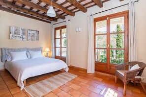Ein Schlafzimmer mit Bett, Sessel, Lampe und Blick durch ein Fenster.