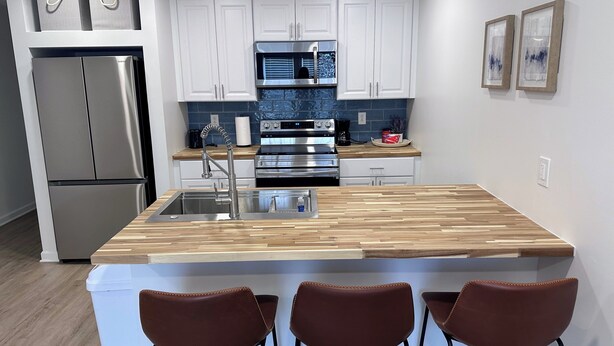 A modern kitchen with a central island, stainless steel appliances, and a white backsplash.