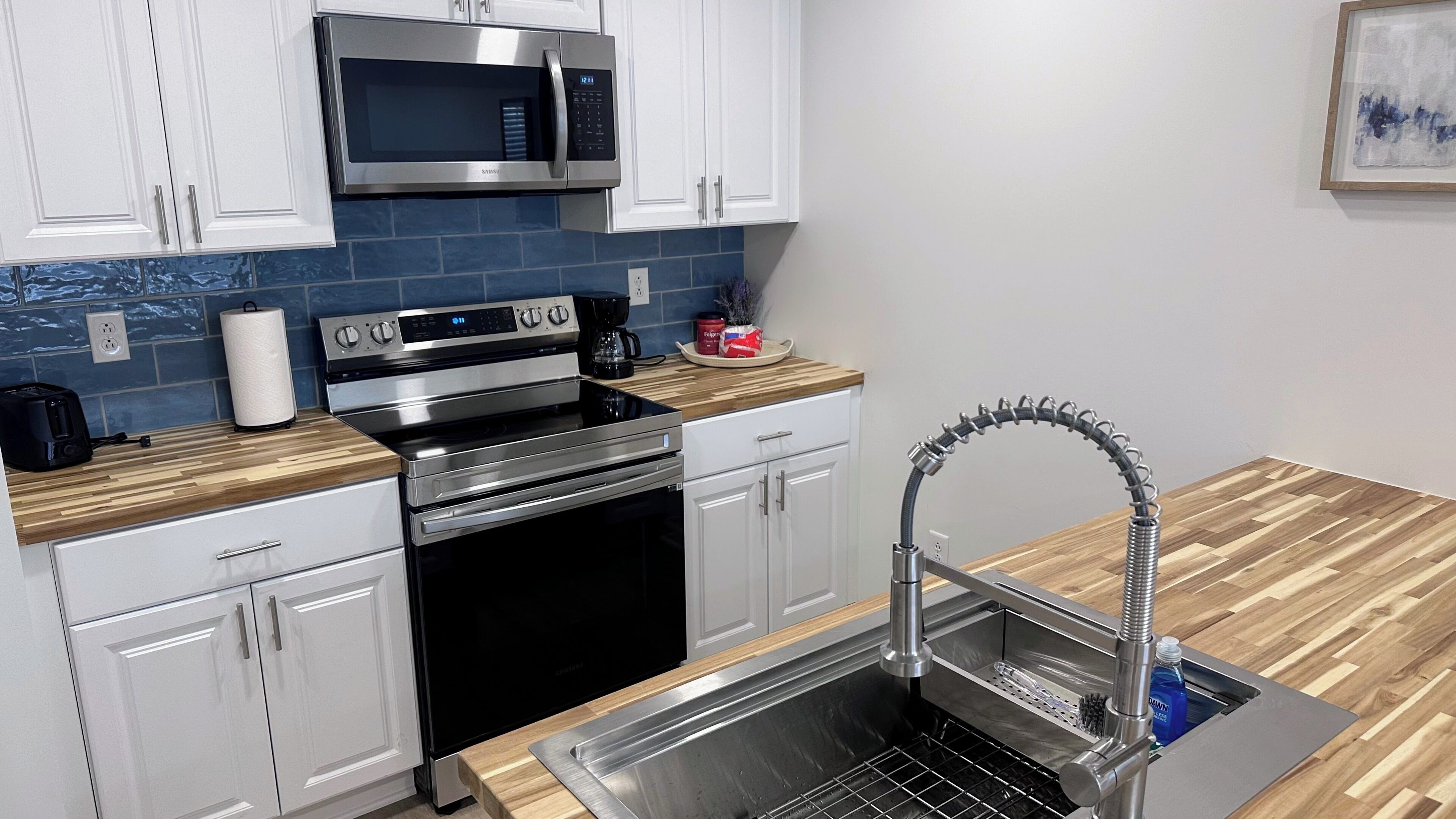 Una cocina moderna con electrodomésticos de acero inoxidable, microondas, tostadora y un lavabo con grifo flexible.