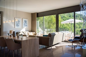 Ein modernes Interieur mit Essbereich, Sitzgelegenheiten und großen Fenstern mit Blick auf Grünflächen.