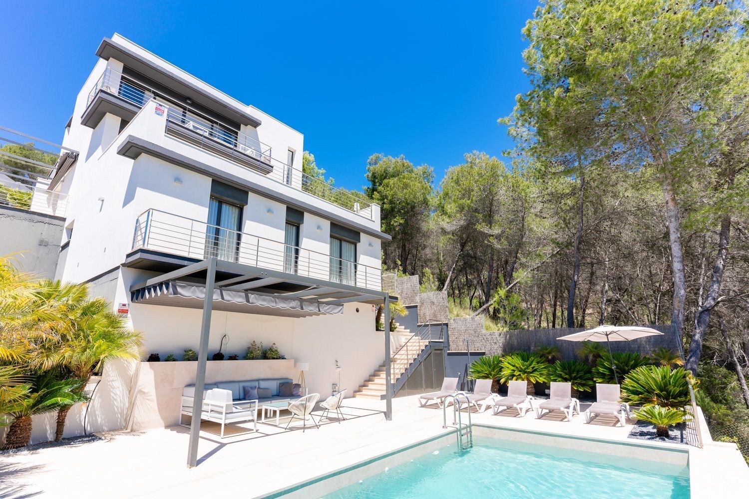 A modern two-story building with a pool, outdoor seating, and a staircase leading to a balcony.