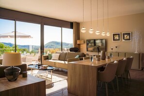 Ein modernes Wohnzimmer mit großem Fenster, einer Couch, einem Essbereich und einem Fernseher.
