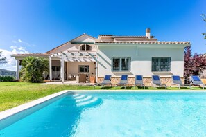 Una casa de dos pisos con piscina, mobiliario exterior y una pérgola.