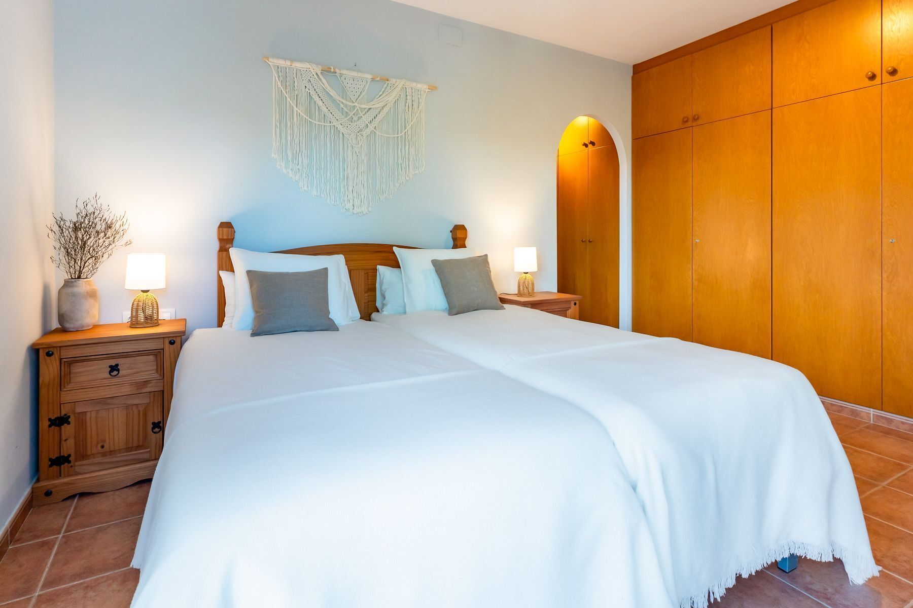 A neatly made bed with a white bedspread, a wooden headboard, and two bedside tables with lamps.
