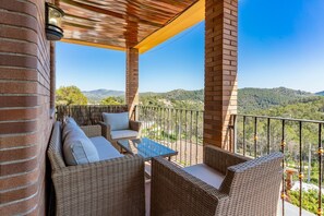 Ein Balkon mit Korbmöbeln, einem Glastisch und Blick ins Grüne.