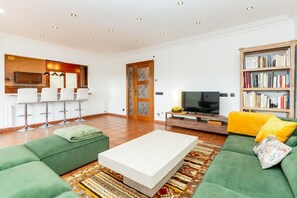 Ein modernes Wohnzimmer mit einer Couch, einem Couchtisch, einem Fernseher, einem Bücherregal und einer Küchenzeile mit Barhocker.