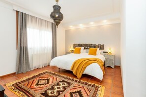 Ein Schlafzimmer mit einem Bett, einem gemusterten Teppich, einem Wanddekor und einer Pendelleuchte.