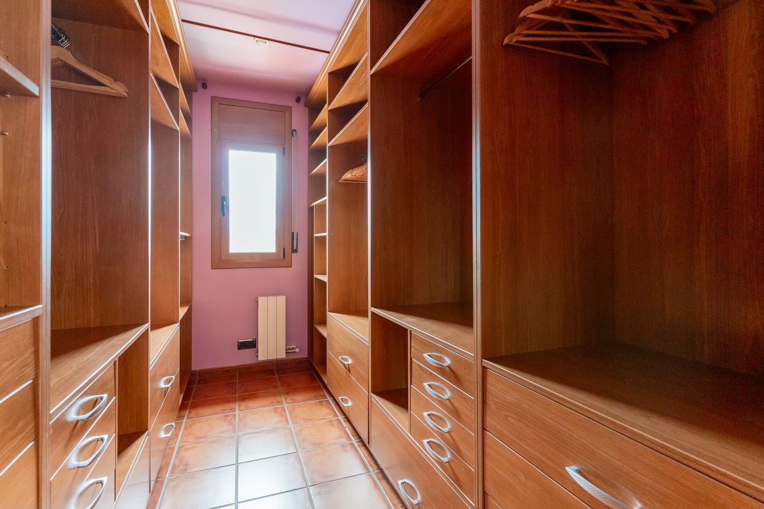 Een inloopkast met houten planken en lades, een radiator en een raam met natuurlijk licht.