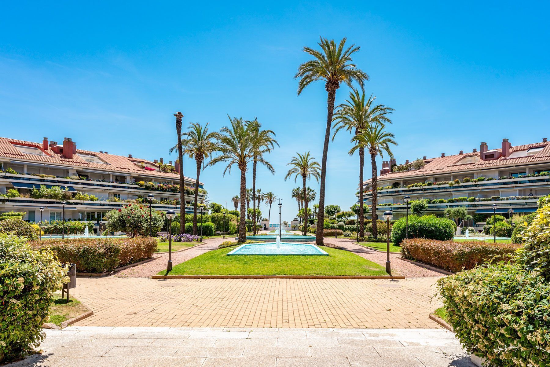 A hotel courtyard with a central fountain, palm trees, and a brick pathway.