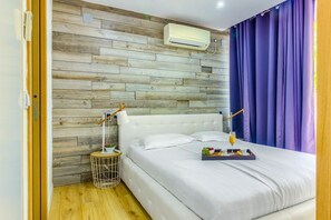 A bedroom with a wooden wall panel, a white bed, a bedside table with a lamp, and a tray with breakfast items.