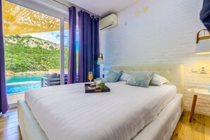 Ein Schlafzimmer mit einem großen Bett, einem Nachttisch, einem Fenster mit Vorhängen und Blick auf eine natürliche Landschaft.