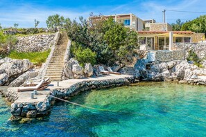 Ein Küsteneigentum mit einer Steintreppe, die zu einem Poolbereich führt, mit klarem, blauem Wasser und einem modernen Haus mit Steinaußenwand.