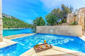 Ein Schwimmbecken mit einem Tablett Frühstücksvielfalt, umgeben von Steinmauern und Blick auf eine Küstenlandschaft.