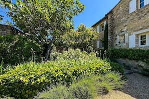 Ein Steinhaus mit einem Garten davor, einschließlich verschiedener Pflanzen und einem Kiesweg.