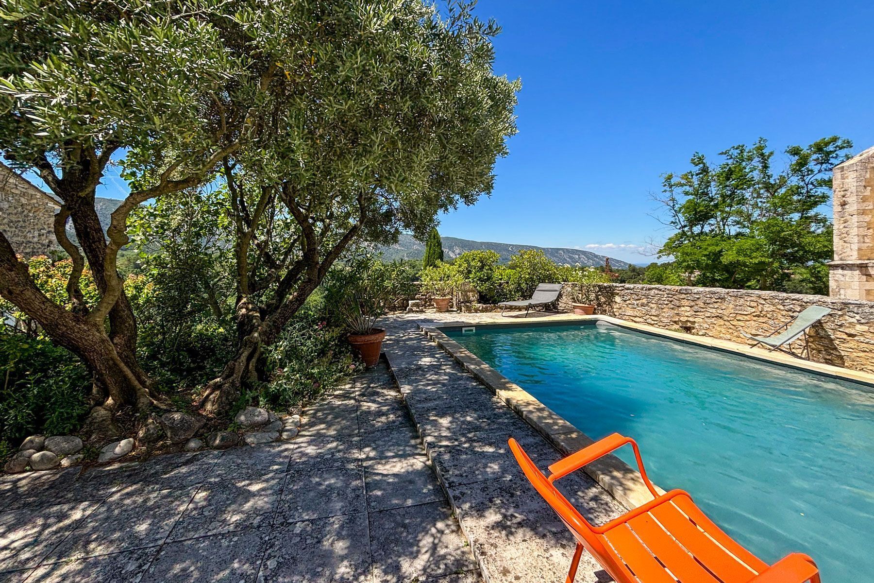 A pool area with stone walls, a tree, and a clear view of the mountains.