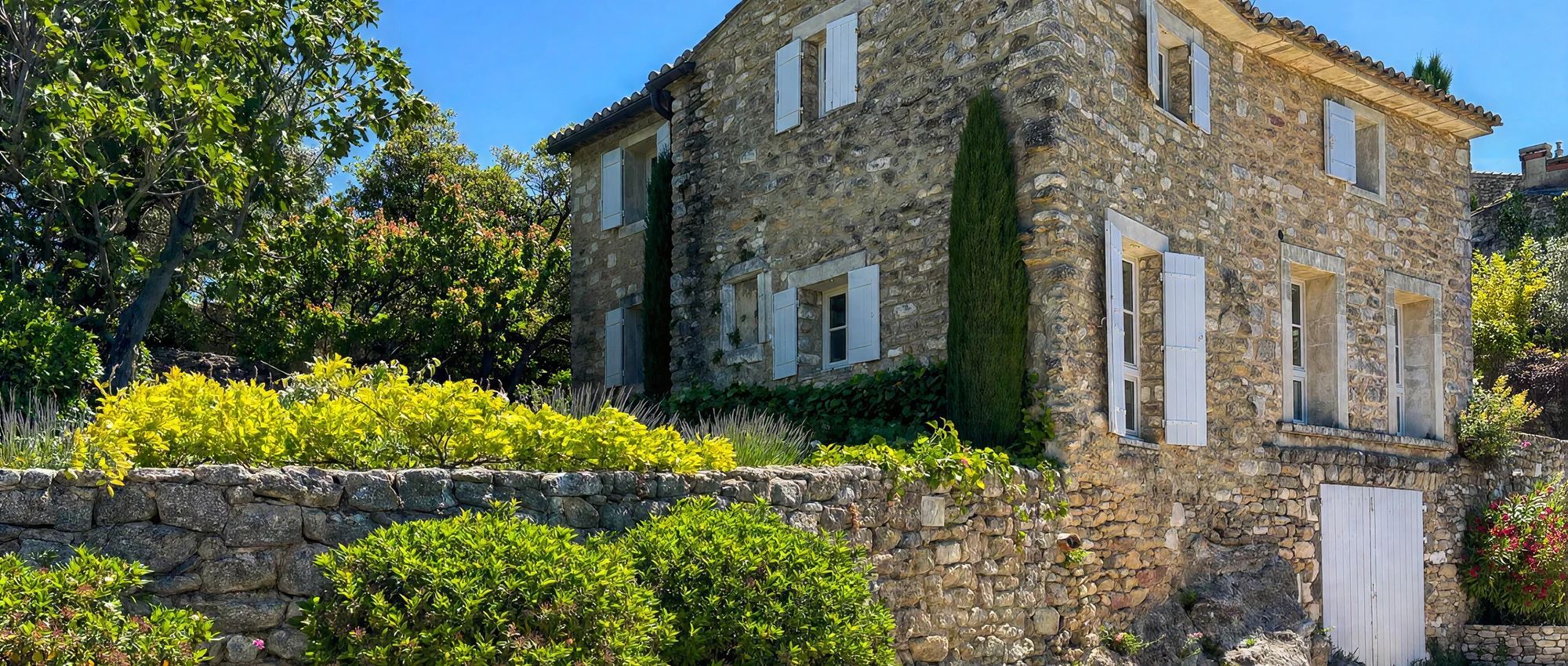 Un bâtiment en pierre doté de nombreuses fenêtres et d’un mur en pierre à l’avant.