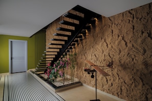A staircase with wooden steps and metal railings, a wall with a textured surface, and a small garden area with pink flowers.
