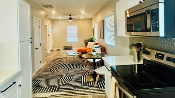 A kitchen with a microwave, oven, and stove. There is a dining area with a table and chairs. - Stylish Downtown Cottage near Alamodome, Hemisphere & Riverwalk (San Antonio)