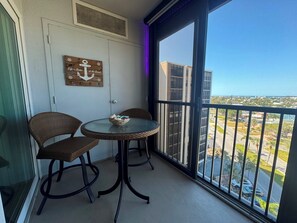 Ein Balkon mit zwei Korbstühlen, einem kleinen runden Tisch und Blick auf Stadt und Meer.