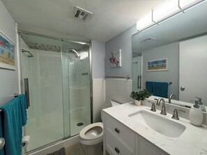Ein Badezimmer mit einer Duschkabine, einer Toilette, einem Waschbecken mit Spiegel und einer Zimmerpflanze.