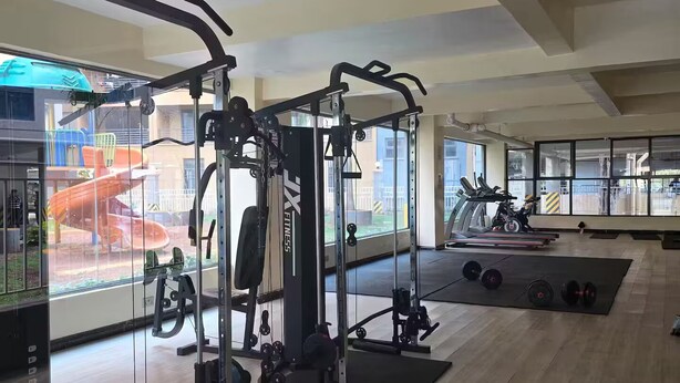 Een sportschool met trainingsapparatuur, loopbanden en uitzicht op een speeltuin door grote ramen.