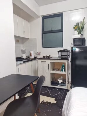 A compact kitchen with white cabinets, a black countertop, a small dining table, and a black refrigerator. - Small Haven (Nairobi)