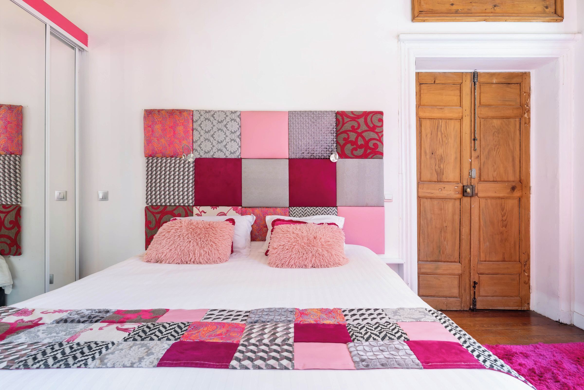 A bedroom with a bed, a quilt, a headboard with patterned panels, and a wooden door.