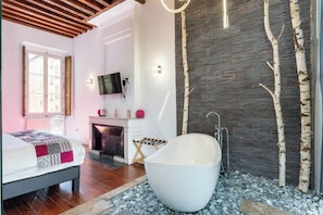 Un dormitorio moderno con una cama grande, una bañera, una chimenea y una pared de piedra con abedules.