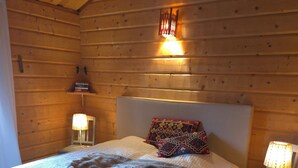 Une chambre à coucher dans un chalet en bois, avec un lit, deux lampes de chevet, une tête de lit et un luminaire fixé au mur.