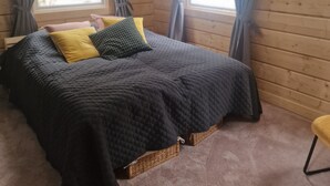 Un dormitorio acogedor con una cama grande, dos ventanas con cortinas, una lámpara de techo y suelo de madera.