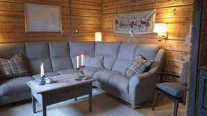 Un acogedor interior de cabaña con techo de madera, un sofá gris, una mesa de centro de madera con velas y un tapiz colgado en la pared.