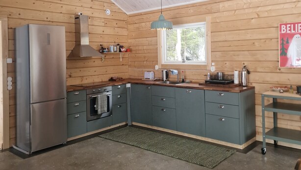 Une cuisine moderne avec des murs en bois, un réfrigérateur en acier inoxydable, un four encastré et une fenêtre donnant sur les arbres.