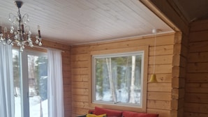 L’intérieur d’un chalet accueillant, avec un canapé rouge, une table basse en verre, une chaise en bois et un lustre.