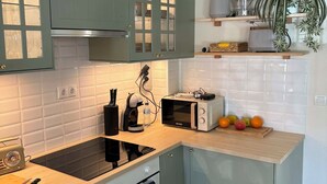 Une cuisine moderne équipée d’une cuisinière intégrée, d’un four à micro-ondes et d’une machine à café. On y trouve des placards avec des portes en verre, un plan de travail agrémenté d’un panier de fruits et une plante en pot posée sur une étagère.