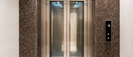 An elevator with a digital display showing the number 4, surrounded by a speckled granite wall.