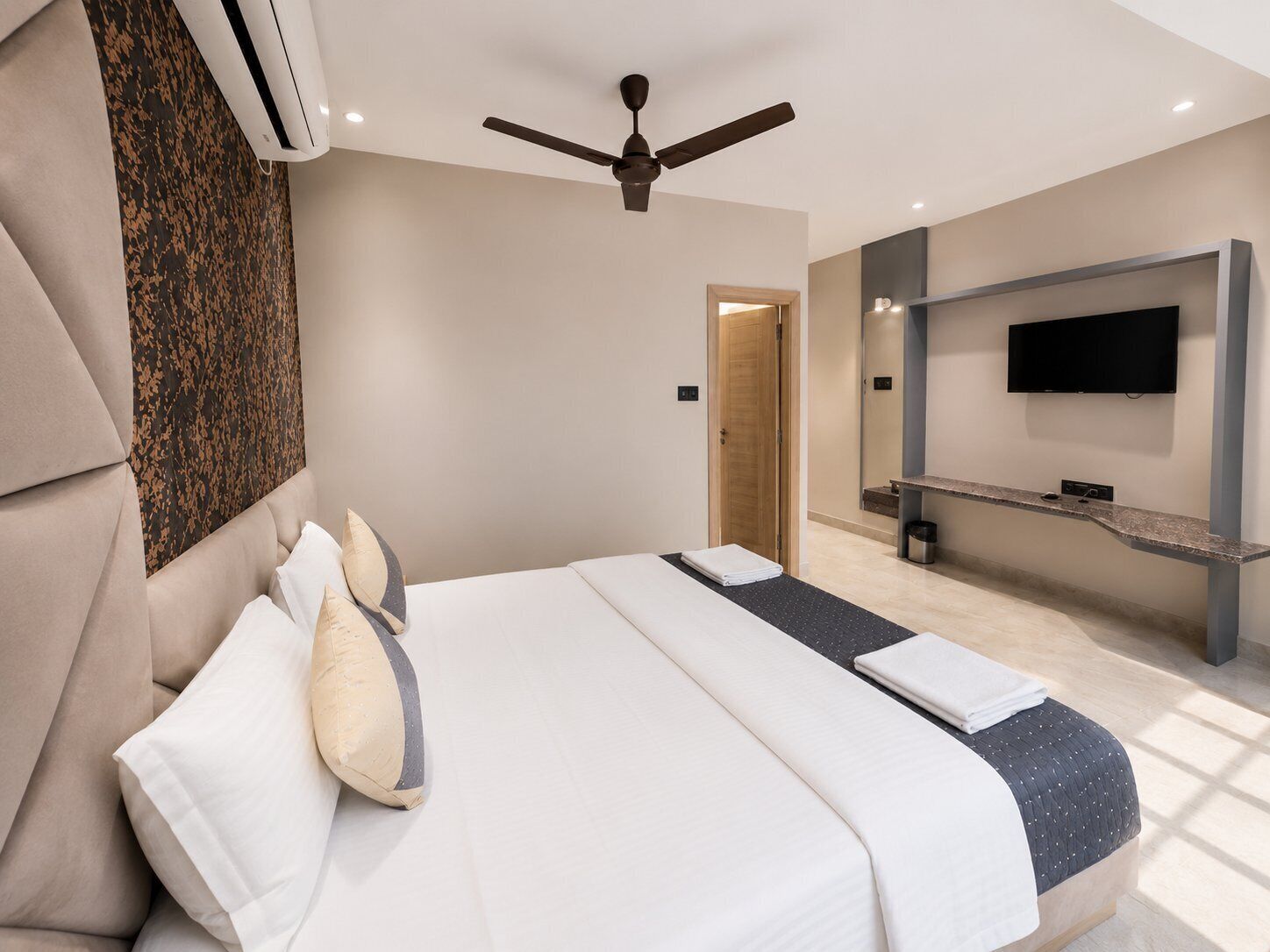 Habitación de hotel moderna con cama, ventilador de techo, televisor de pantalla plana y un baño pequeño.
