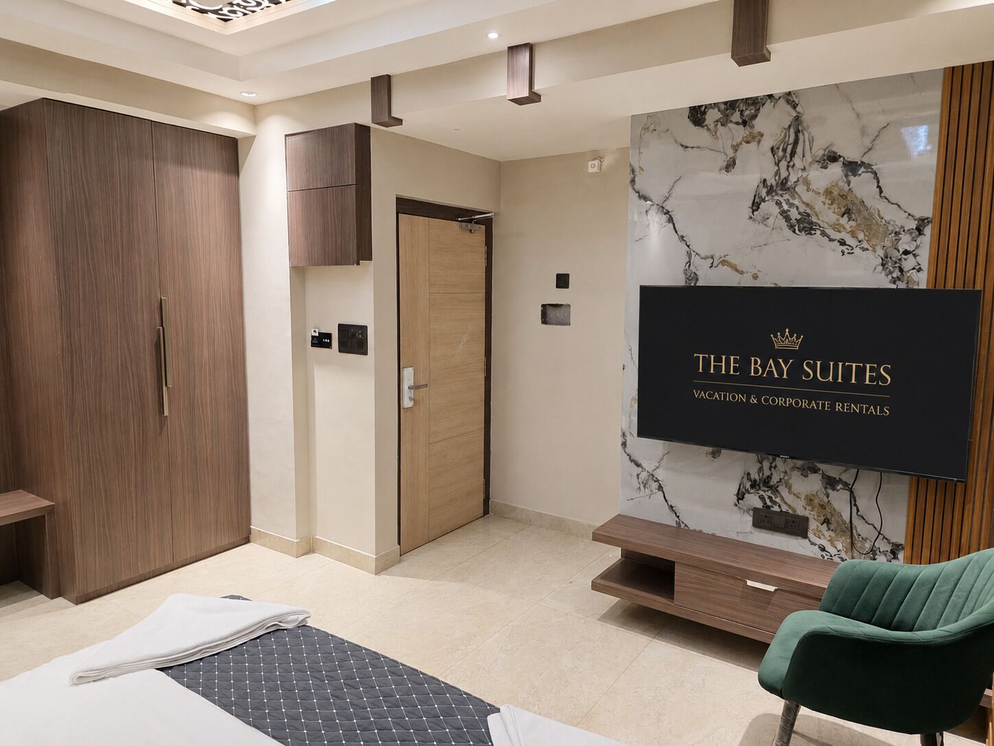 Habitación de hotel con cama, una silla verde, armario, televisor y pared de mármol.