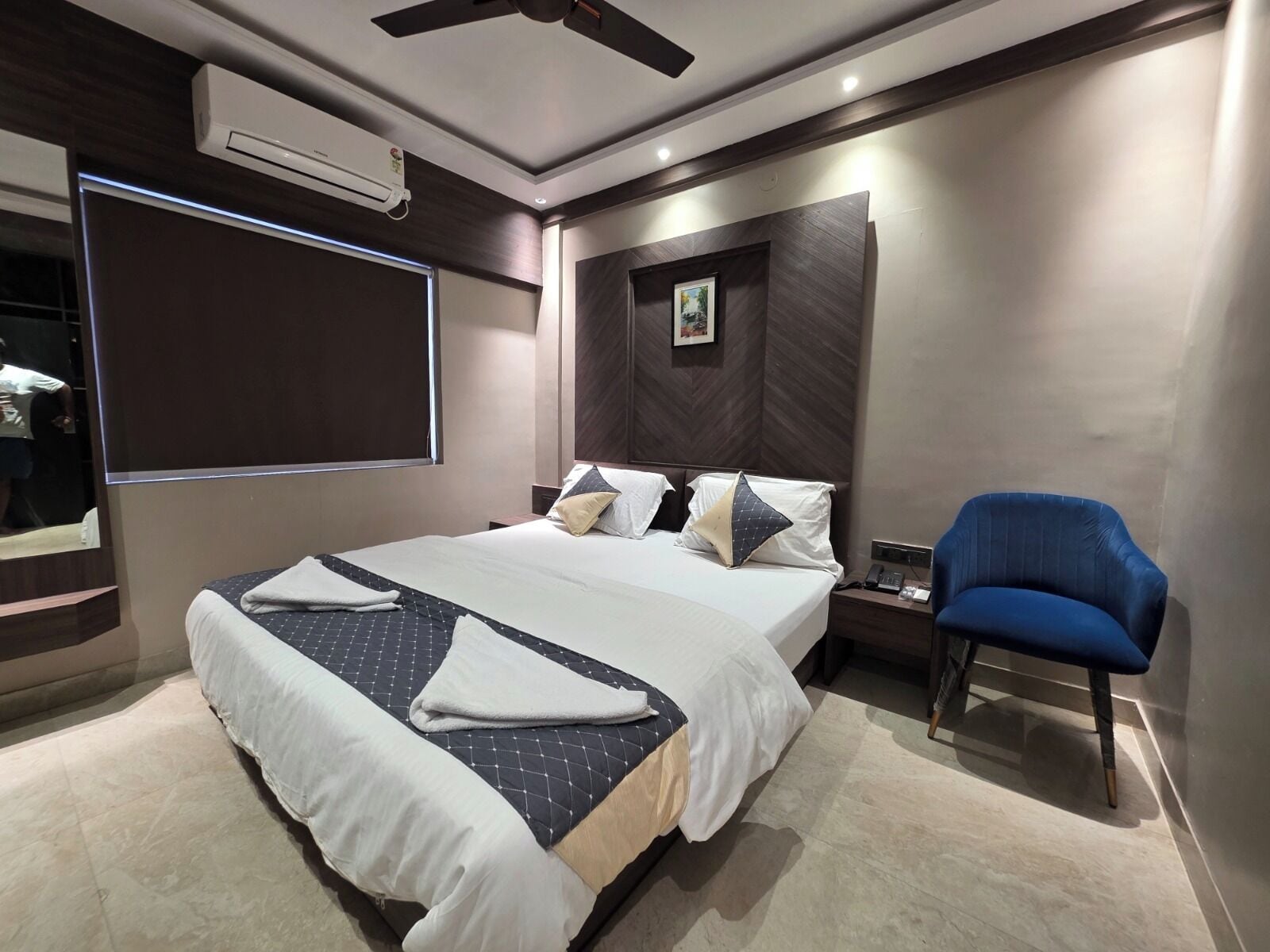 A modern hotel room with a large bed, a chair, a nightstand, and a ceiling fan.
