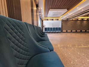 A row of dark green upholstered seating with a quilted pattern, a ceiling with recessed lighting, and a stone wall with a textured finish. - The Bay Suites - NIS (Barasat)