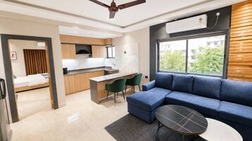 A modern living room with a blue sofa, a small round table, and a kitchen area with a wooden countertop and a built-in oven.
