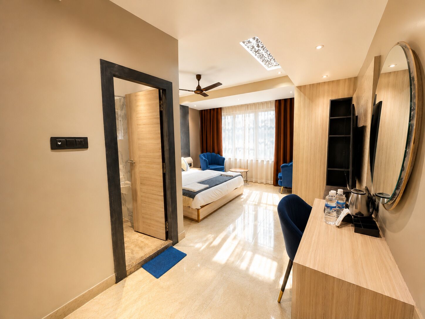 A hotel room with a bed, a desk, a chair, a mirror, and a ceiling fan.