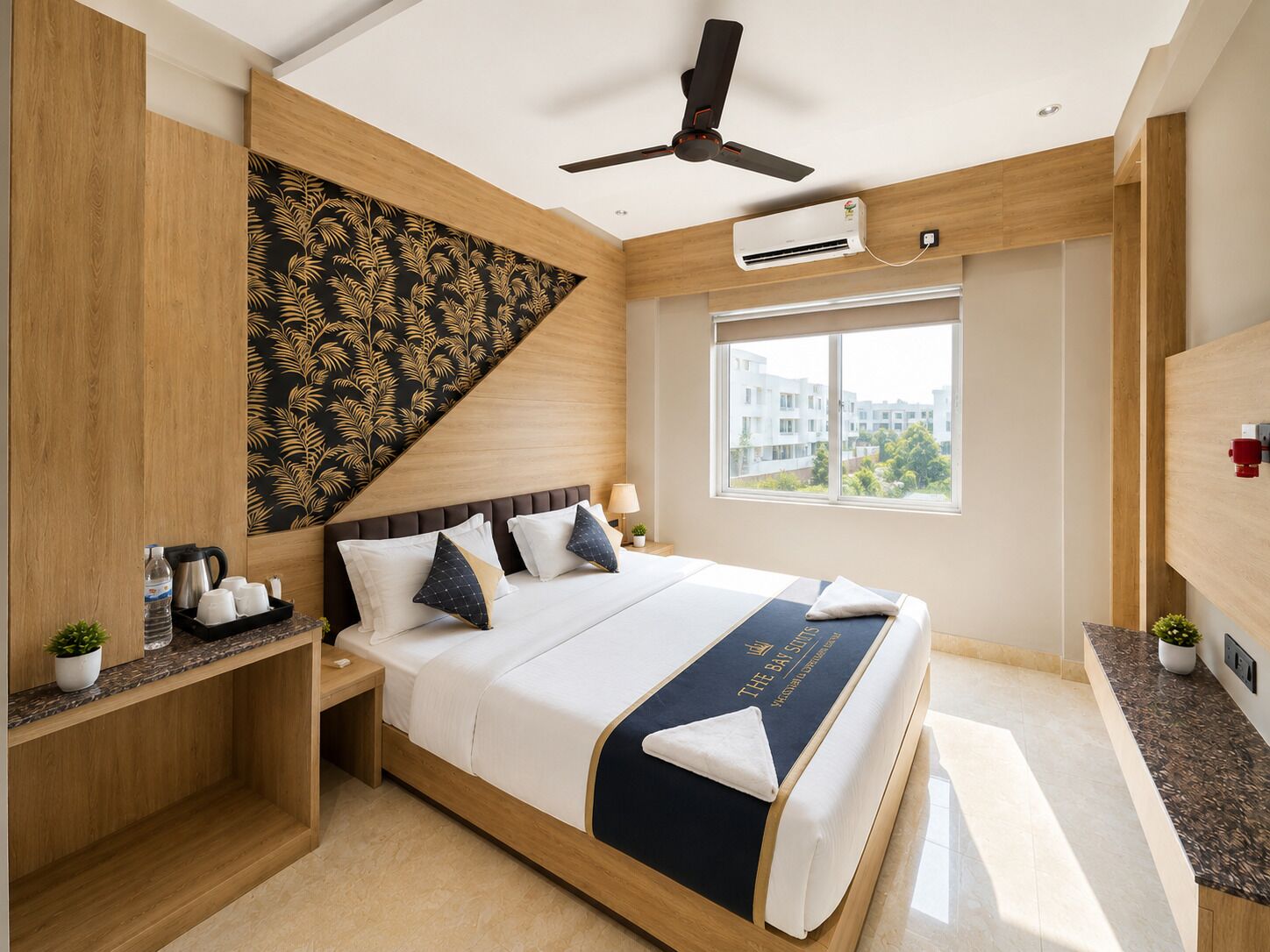 A modern hotel room with a bed, bedside tables, a ceiling fan, an air conditioning unit, and a window with a city view.