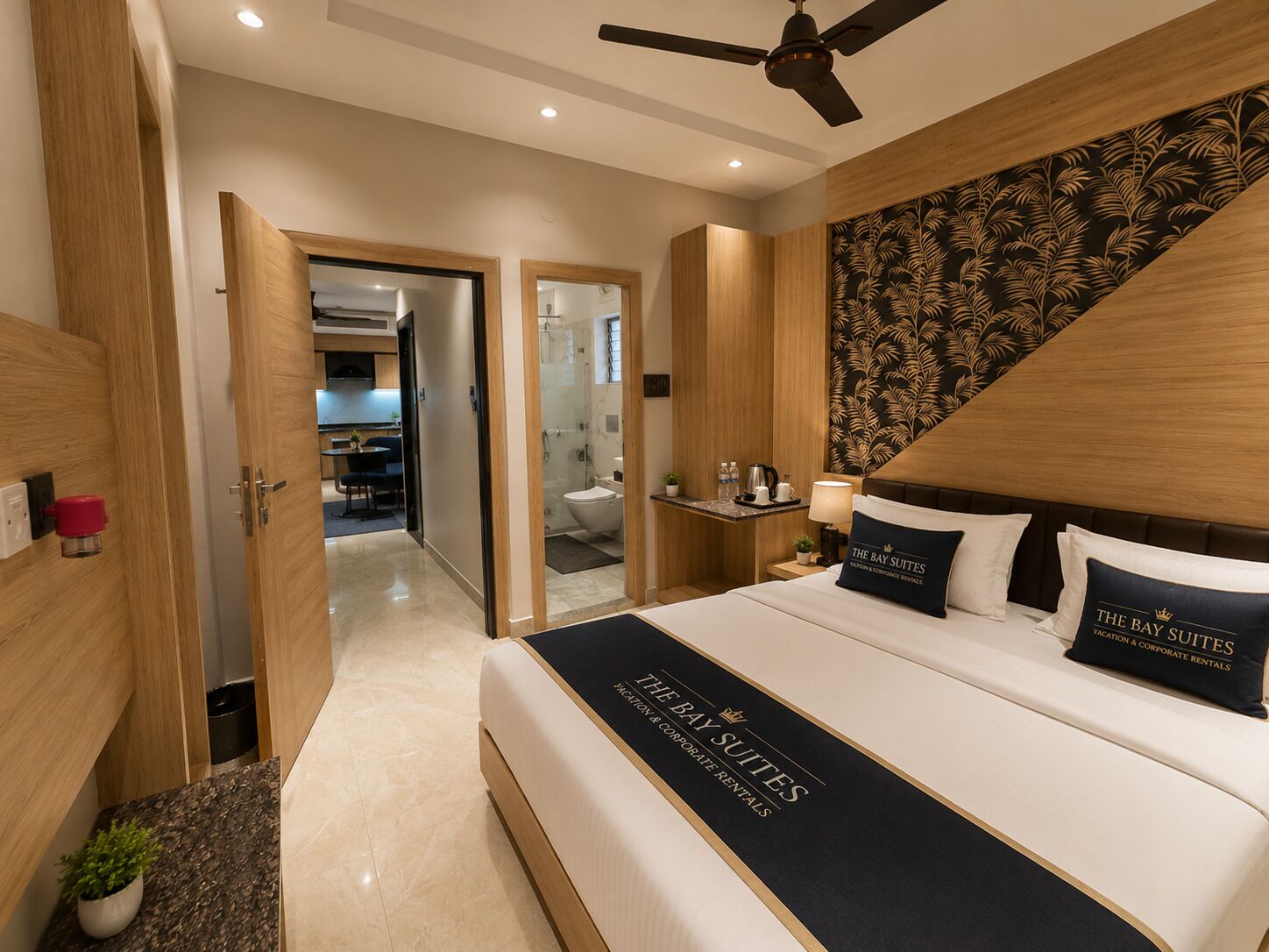 A hotel room with a bed, a ceiling fan, a nightstand with a lamp, and a bathroom visible through an open door.