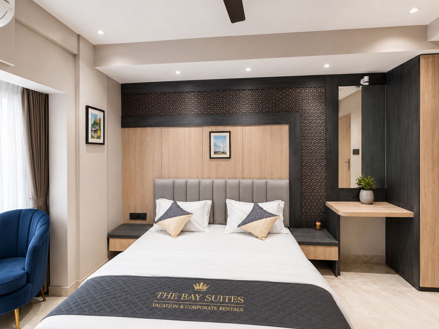 A modern hotel room with a large bed, a blue armchair, a bedside table with a plant, and a wall-mounted mirror.