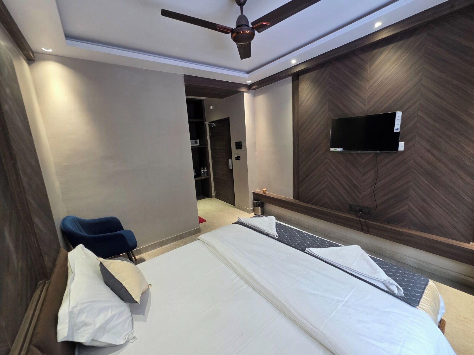 A hotel room with two beds, a ceiling fan, a TV mounted on the wall, and a wardrobe.