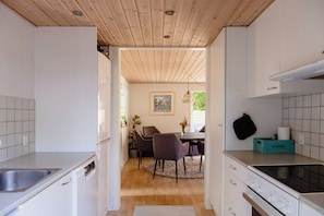 A kitchen with white cabinets, a wooden ceiling, a dining area with chairs and a table, and a storage box labeled 'STORAGE'. - Blue home with room for fun and comfort (Storvorde)