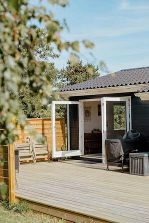 A wooden deck with a grill, a covered seating area, and a wooden fence. - Blue home with room for fun and comfort (Storvorde)