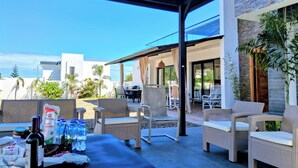 An outdoor patio area with wicker furniture, a table set with bottles and glasses, and a view of the surrounding buildings and sky.