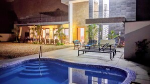 A swimming pool with a tiled edge, outdoor furniture, and a building with a modern design.
